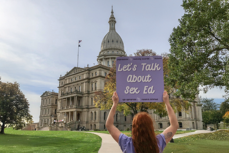 MOASH with sign saying let's talk about sex ed outside michigan capitol building